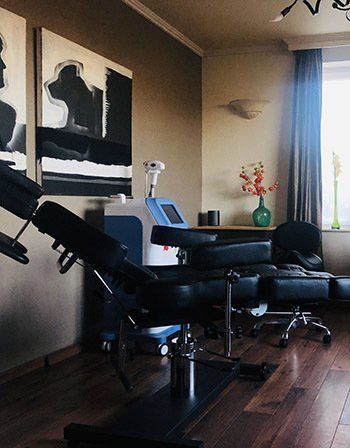Een professionele behandelkamer voor medische esthetiek, voorzien van een verstelbare zwarte behandelstoel en gespecialiseerde apparatuur.