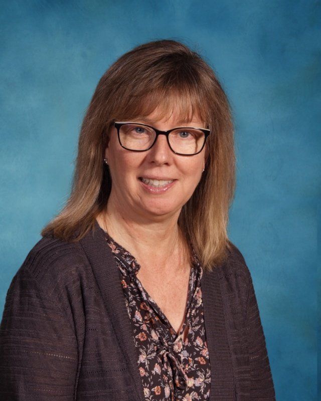 A woman wearing glasses and a brown sweater is smiling for the camera.