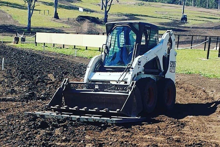 A bobcat is driving through a dirt field.