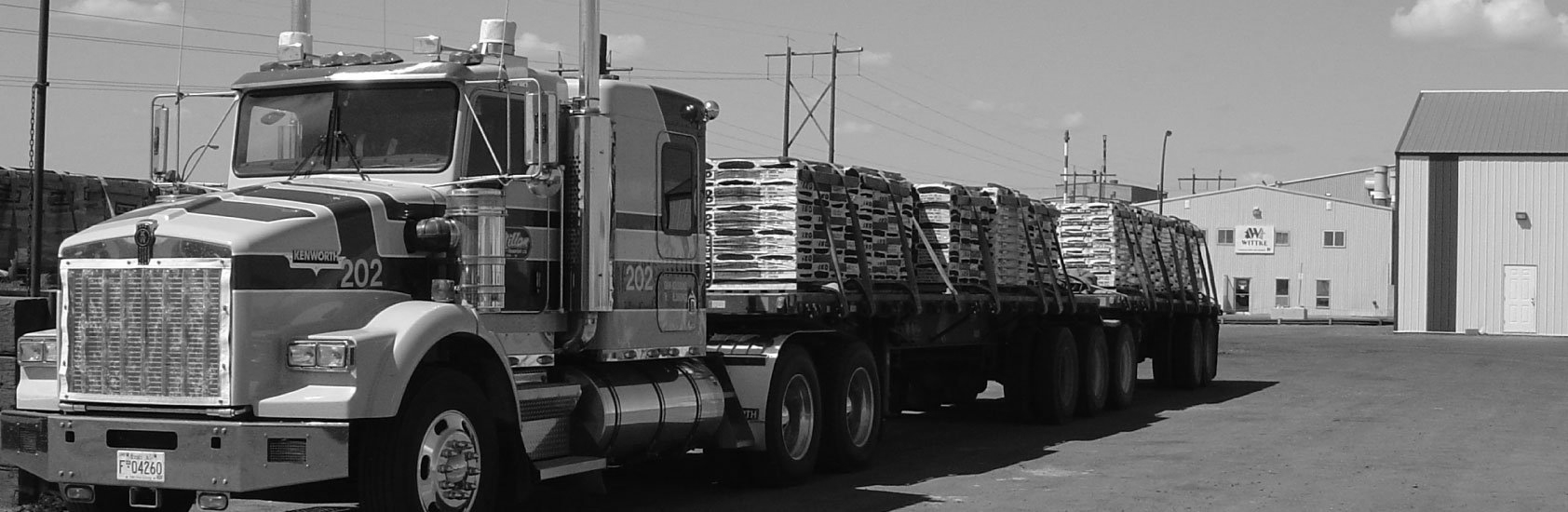 A semi-truck loaded with lumber parked next to a building on a paved lot.