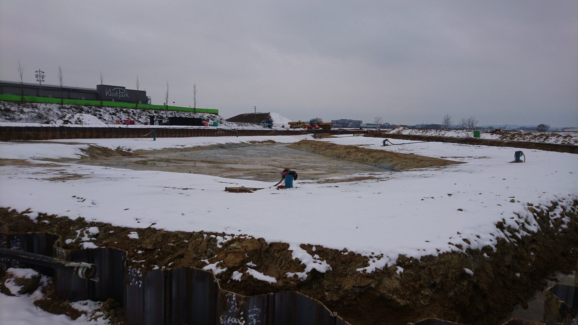 Ein schneebedecktes Feld mit einem Zaun im Vordergrund und einem Gebäude im Hintergrund.