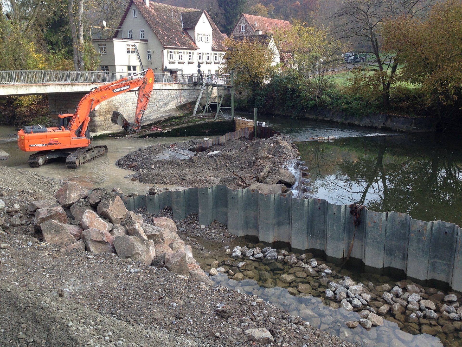 Ein großer orangefarbener Bagger steht neben einem Fluss.