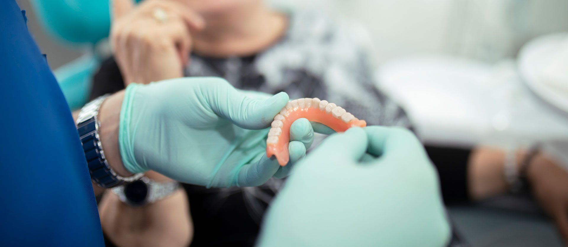 A dentist is holding a denture in front of a patient.