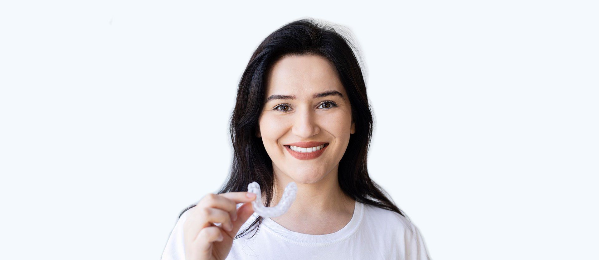 A woman is smiling while holding a whitening device in her hand.