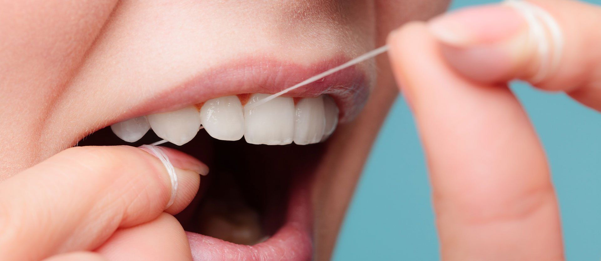 A woman is flossing her teeth with a dental floss.