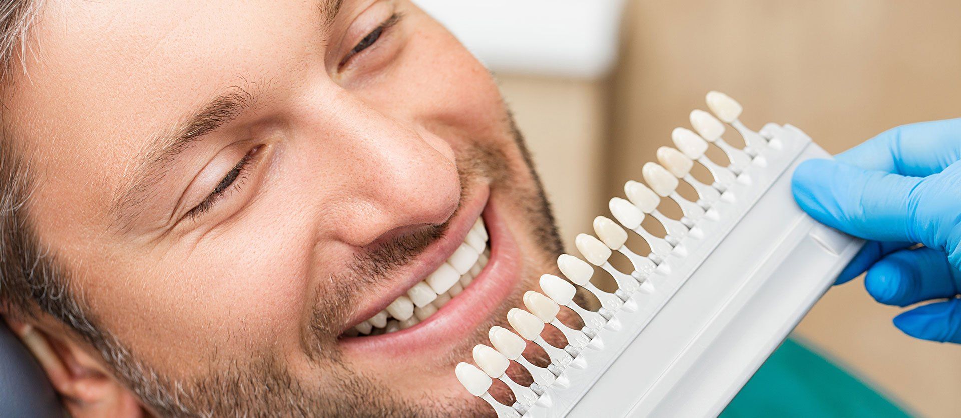 A man is smiling while getting his teeth whitened by a dentist.
