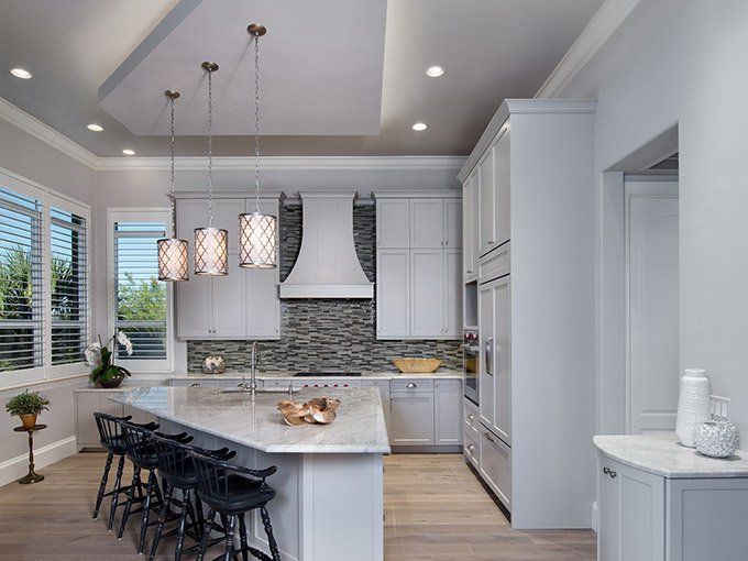 A kitchen with white cabinets, a large island, stools and a ceiling fan.