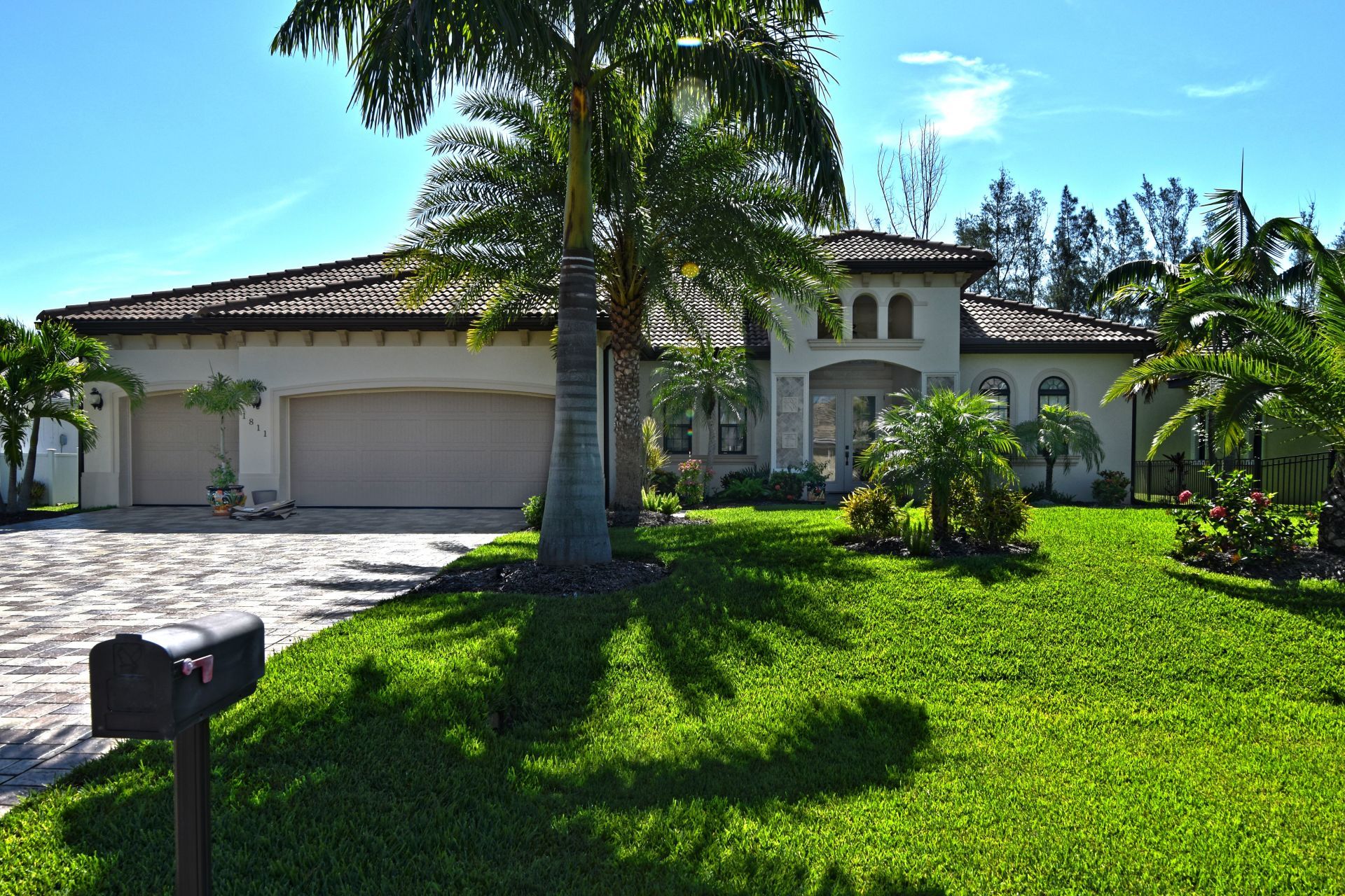 Elegant beige home with tile roof, lush green lawn, palm trees, and a driveway.
