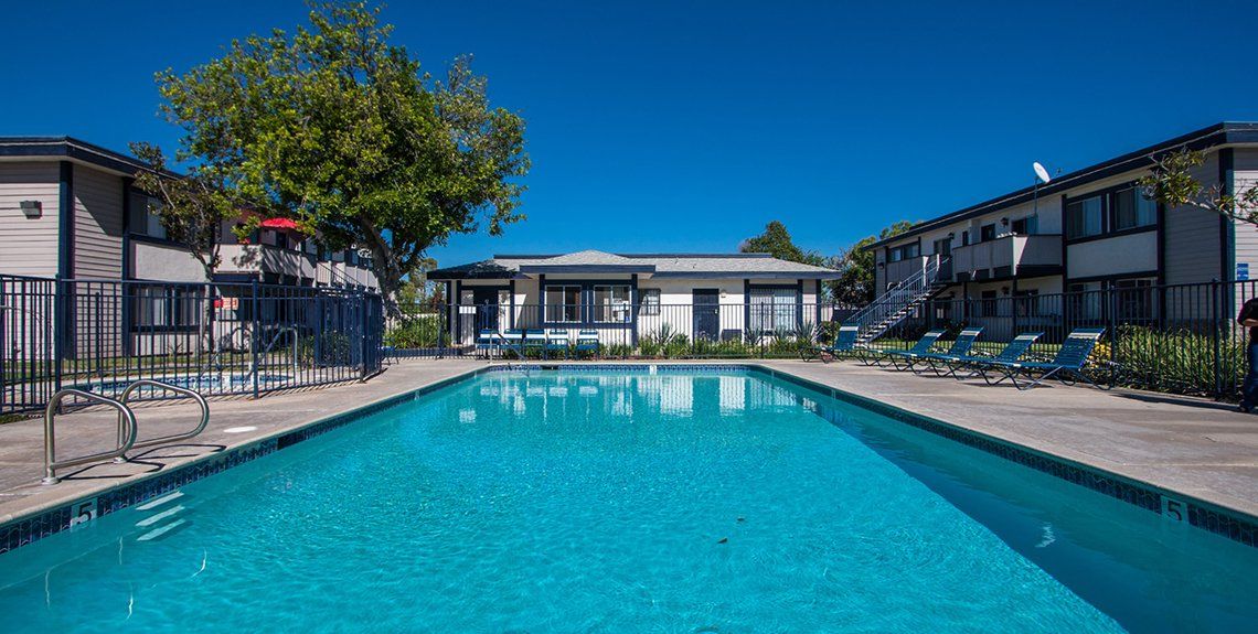 Outdoor apartment complex swimming pool with turquoise water, lounge chairs, and clear blue sky
