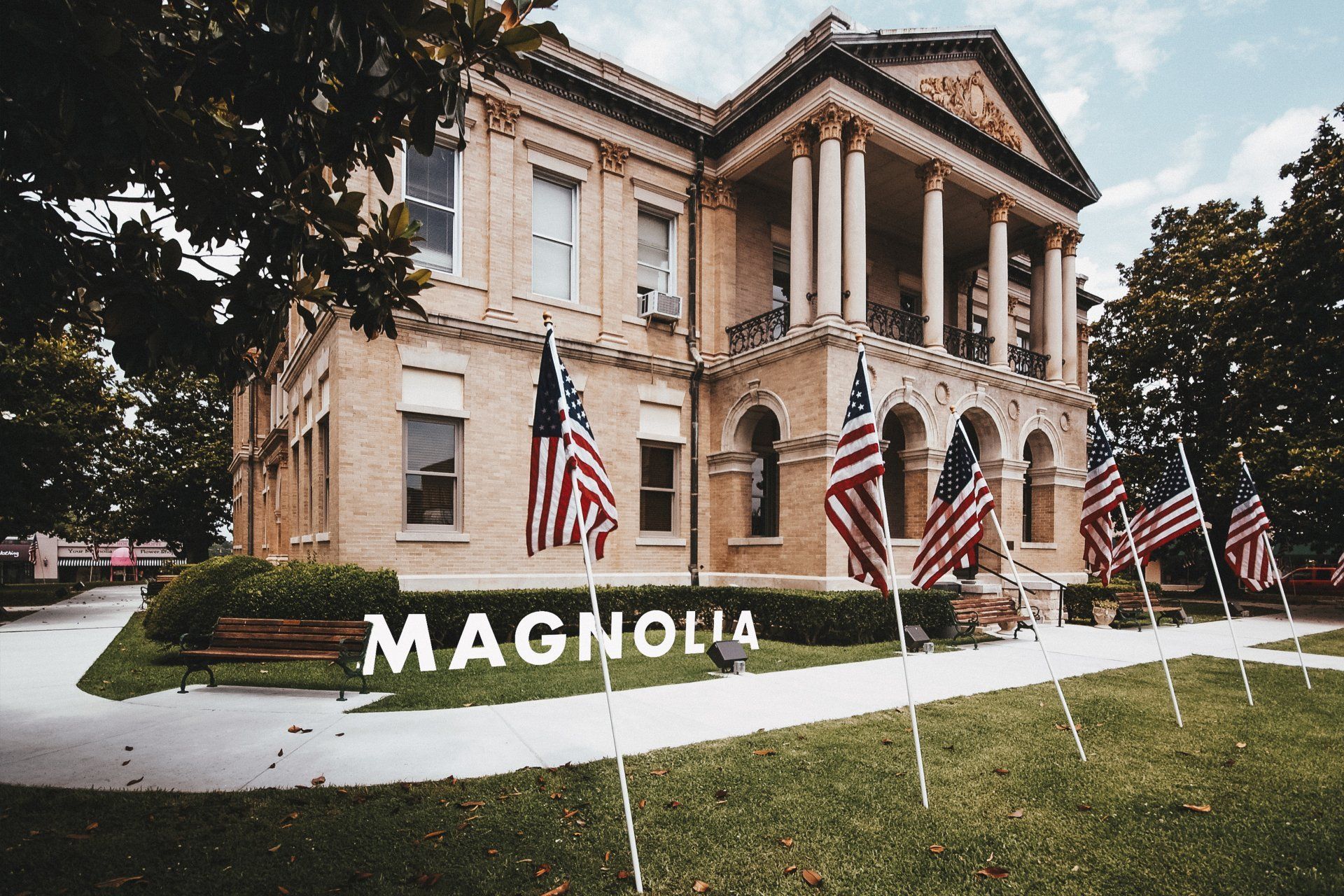 Magnolia building with American flags in front. Beige building with columns and word