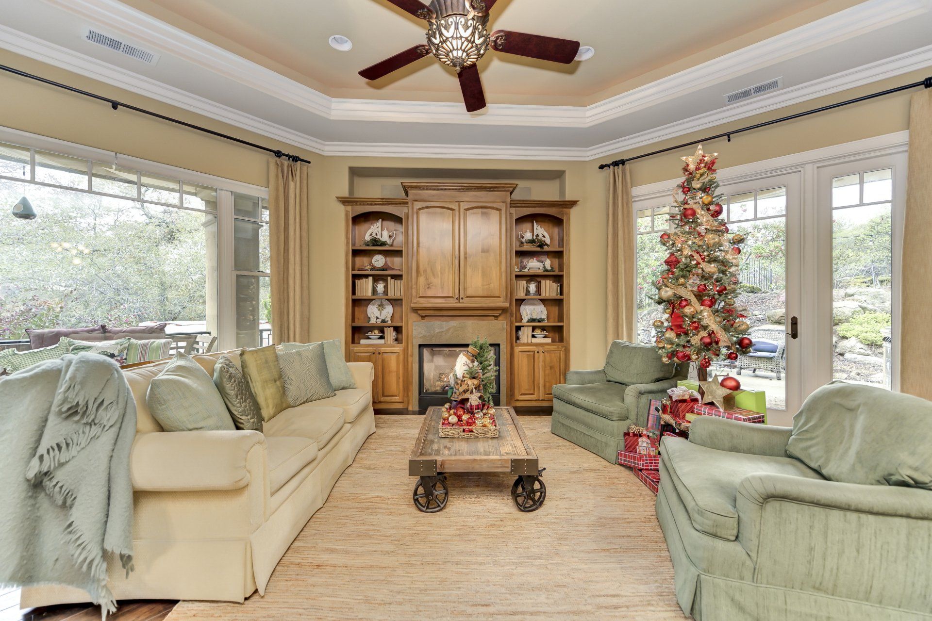 Living room decorated for Christmas with a lit tree, fireplace, and green furniture.