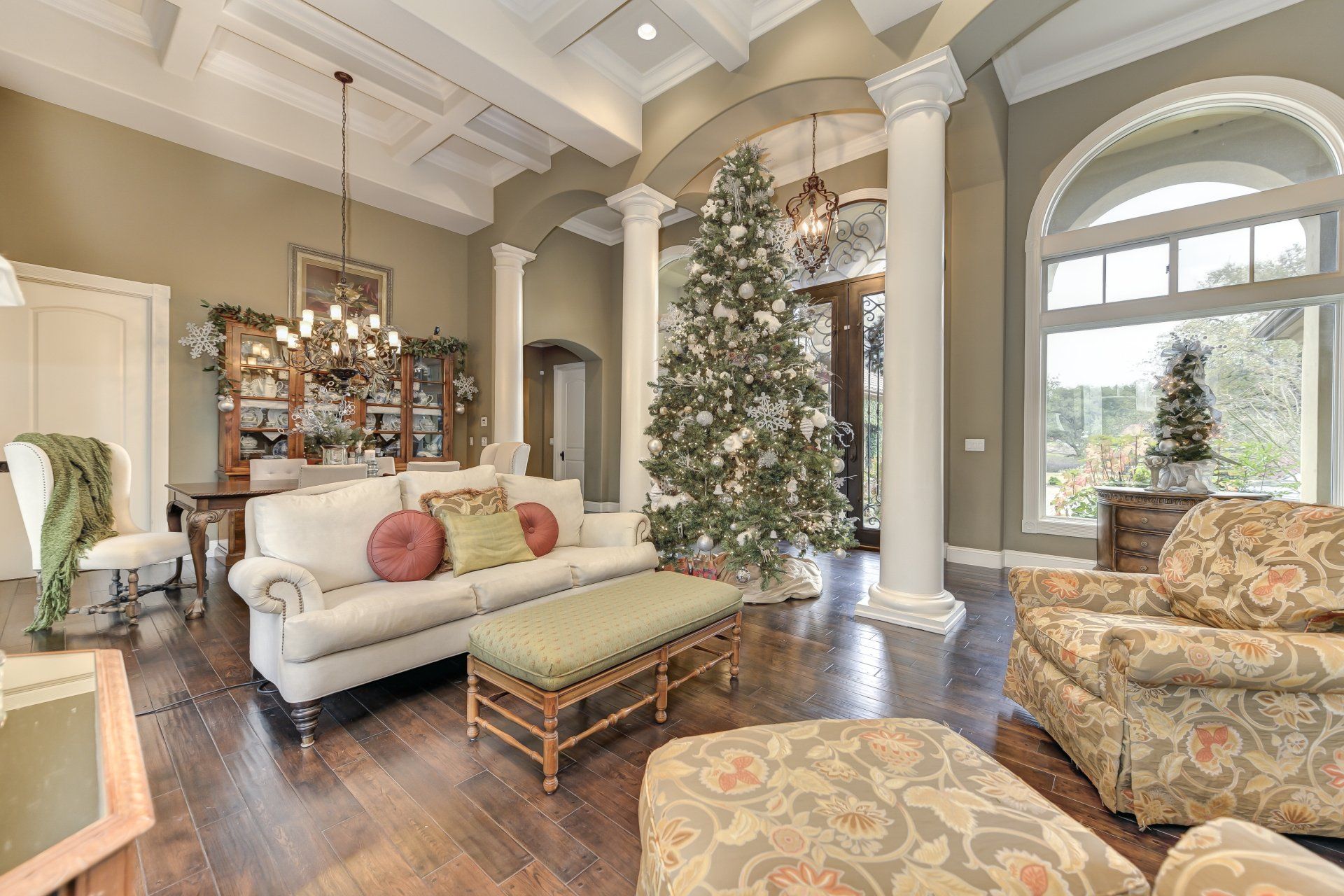 Spacious living room with a decorated Christmas tree, columns, and light-colored furniture.