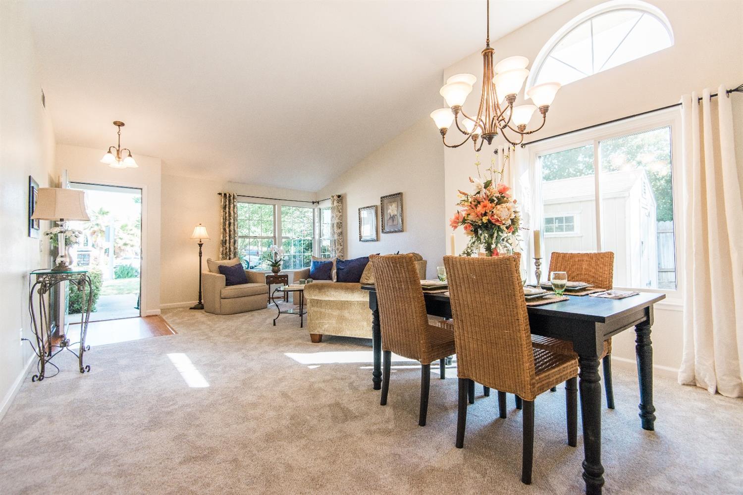 Spacious dining and living room with a table, chairs, sofa, and chandelier, bright natural light.