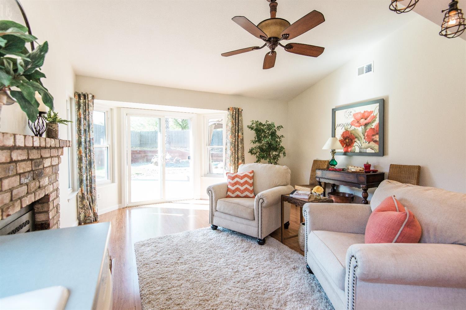 Living room with fireplace, white chairs, rug, and sliding glass doors to backyard.