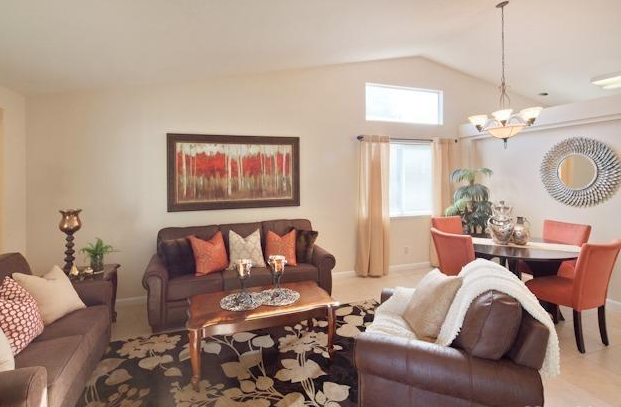 Living room with brown sofas, orange chairs, floral rug, and artwork.