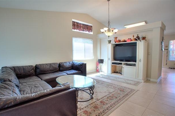 Living room with dark brown sectional sofa, TV, beige walls, and a patterned rug.
