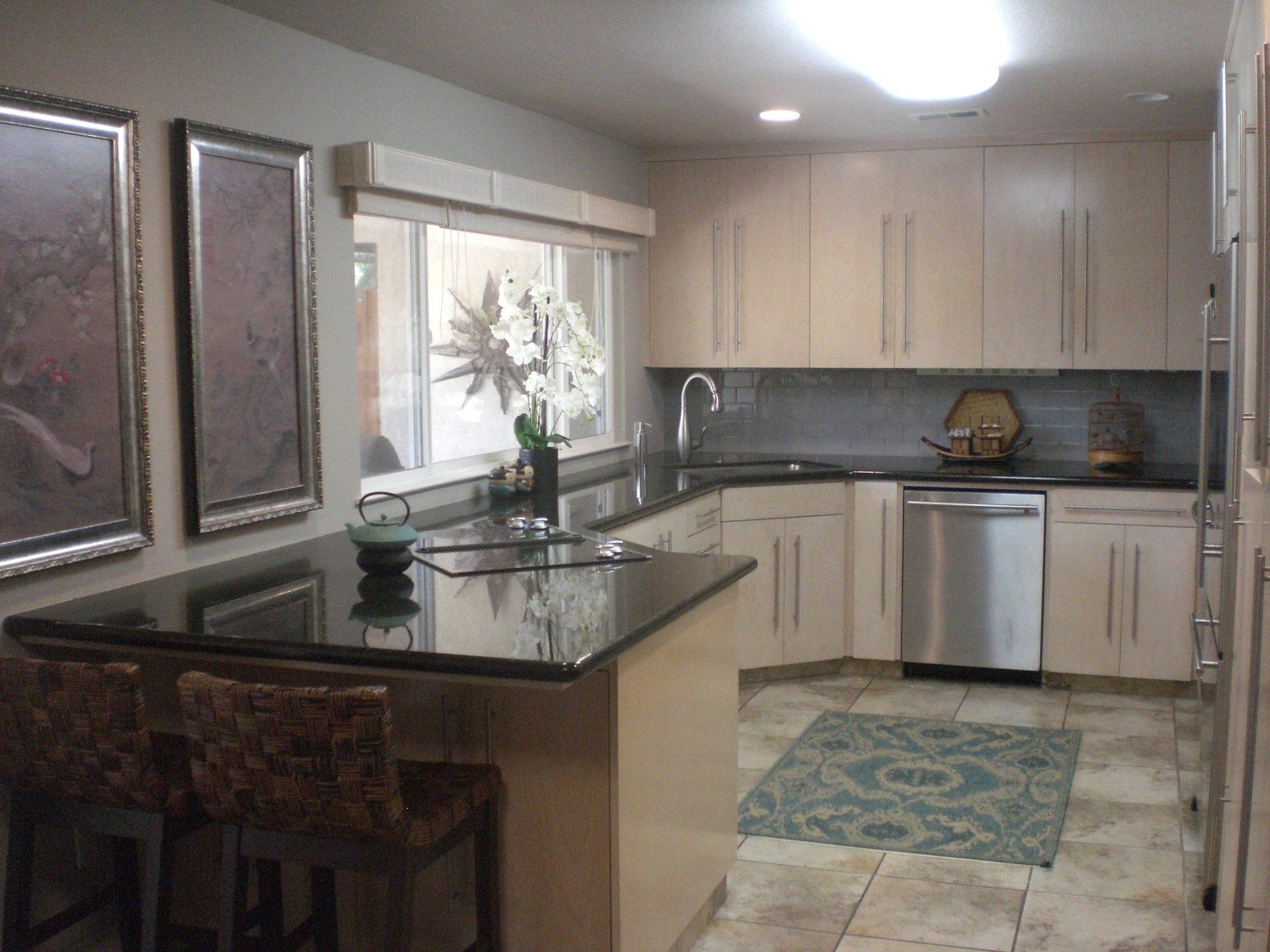 Kitchen with light beige cabinets, dark countertops, island with stools, and stainless steel appliances.