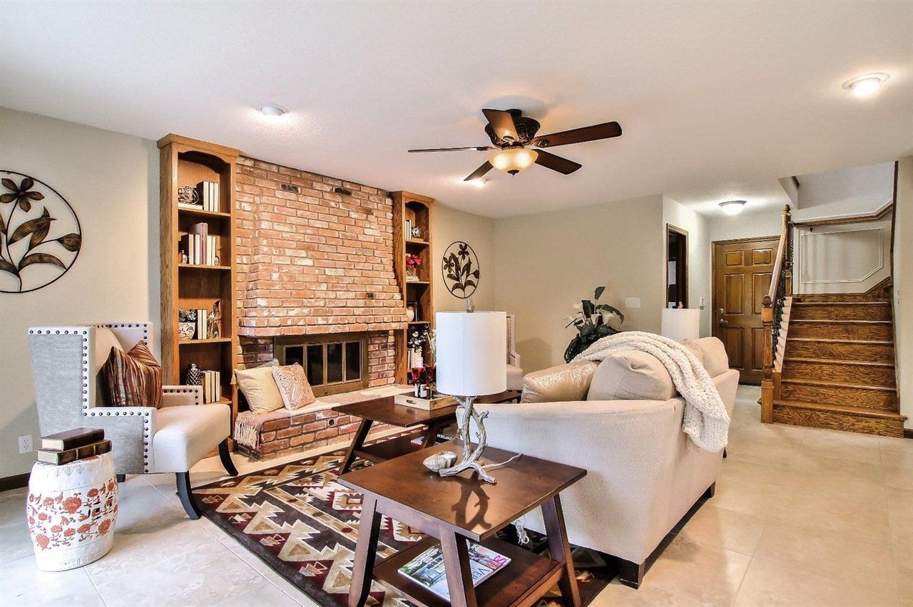 Cozy living room with a brick fireplace, bookshelves, beige sofa, and a wooden staircase.