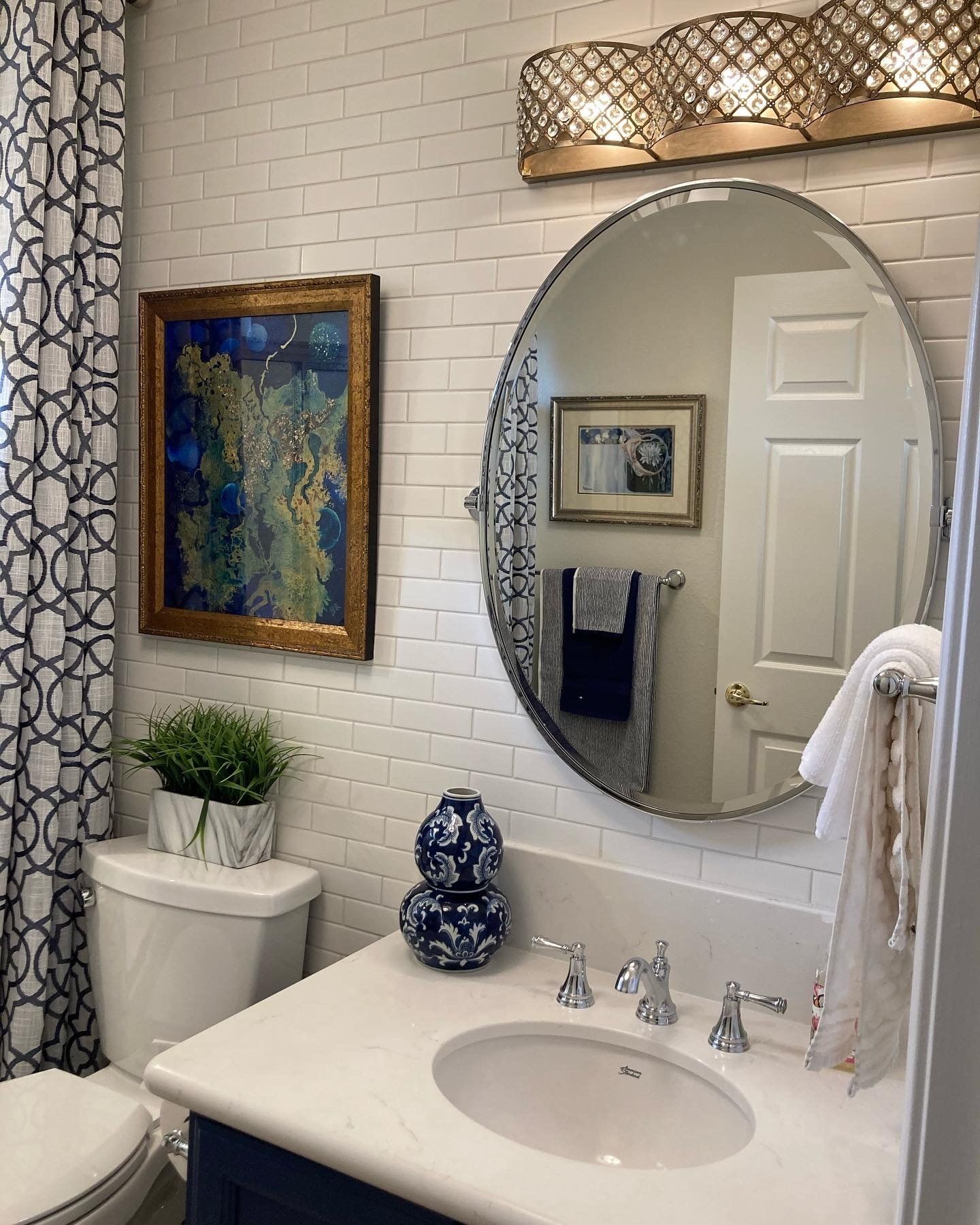 Bathroom with white brick tile, oval mirror, blue and white decor, and gold lighting.