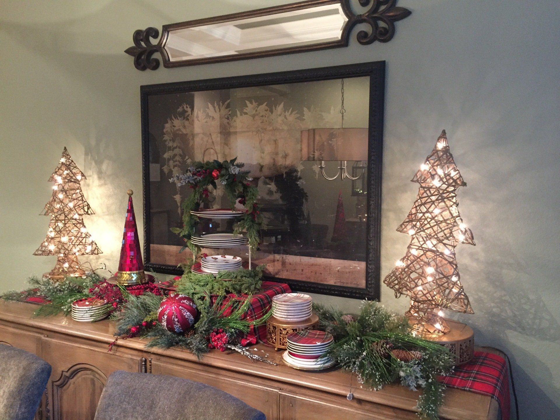 Christmas decorations on a sideboard.  Lit Christmas tree sculptures, garland, and a mirror, on a plaid runner.