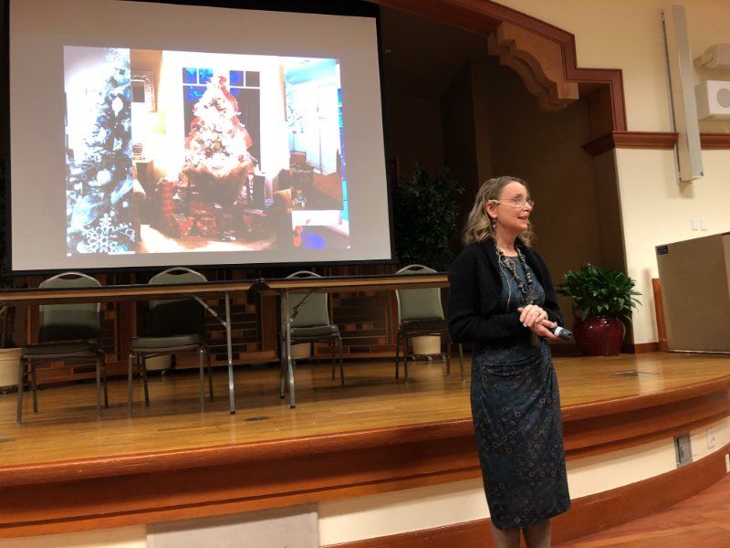 Woman giving a presentation on a stage, image on screen behind her.