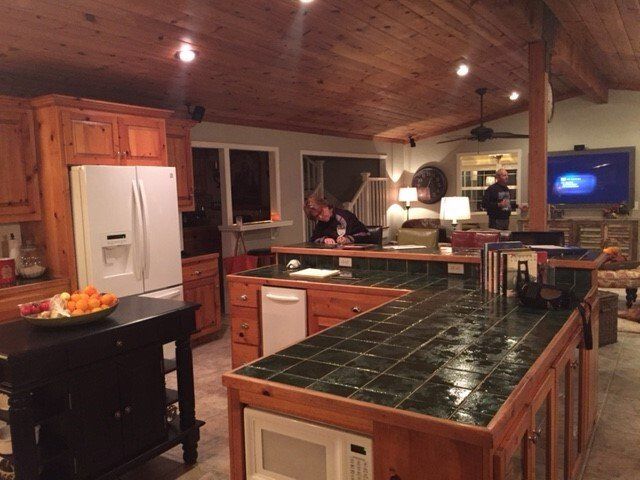 A kitchen with wooden cabinets, a black island, and people near countertops.