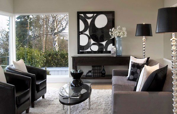 Modern living room: gray sofa, black chairs, abstract art, large window with greenery, and silver accents.