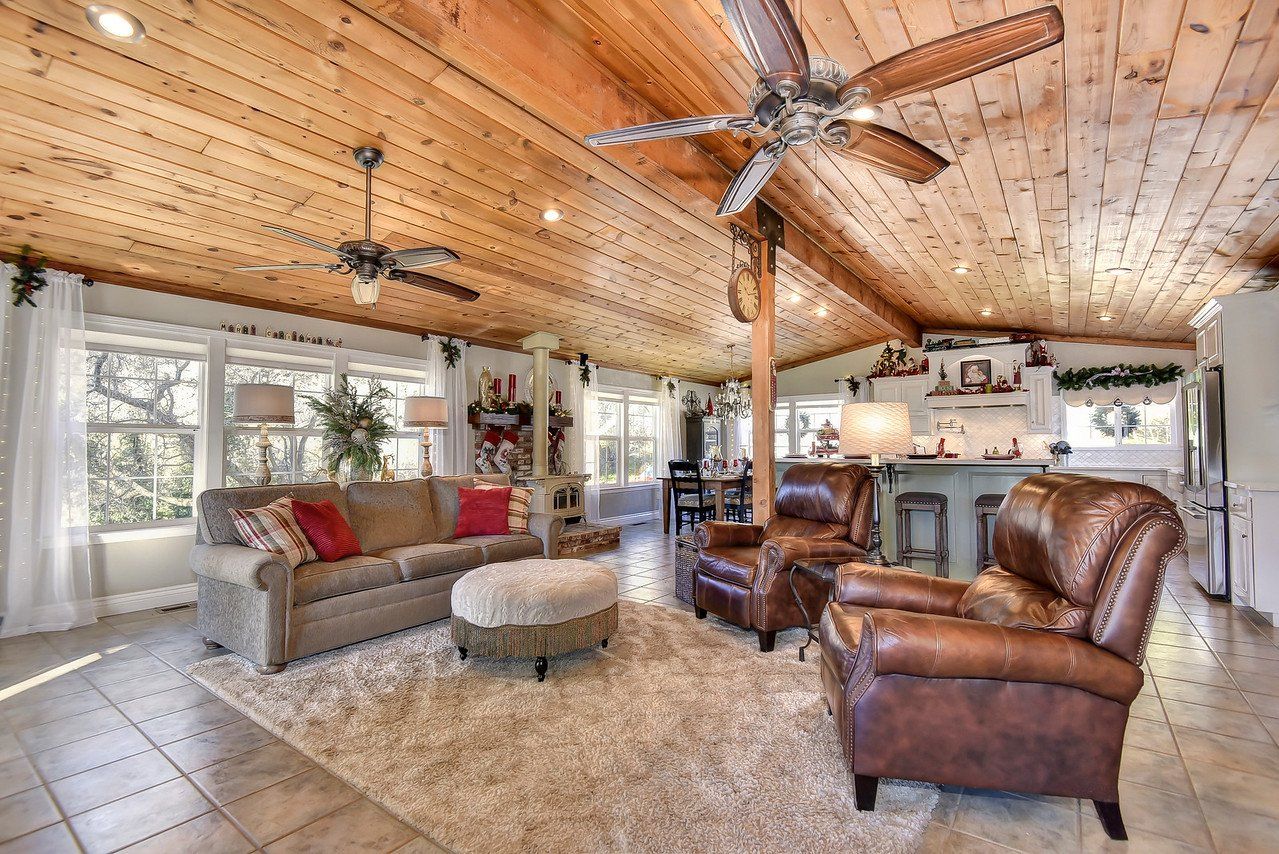 Living room with wood ceiling, tan sofa, brown leather armchairs, rug, and large windows.