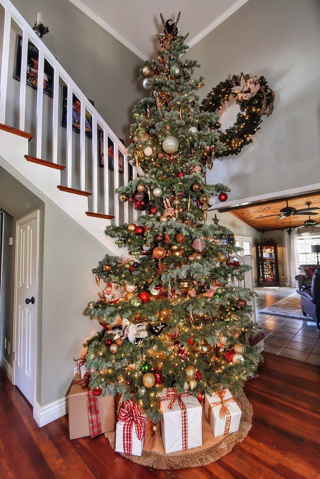Christmas tree decorated with ornaments and lights in a home, with wrapped gifts underneath.