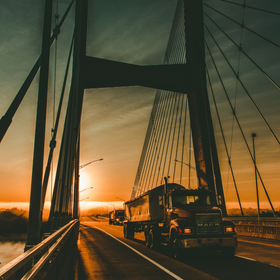 A truck is driving under a bridge at sunset