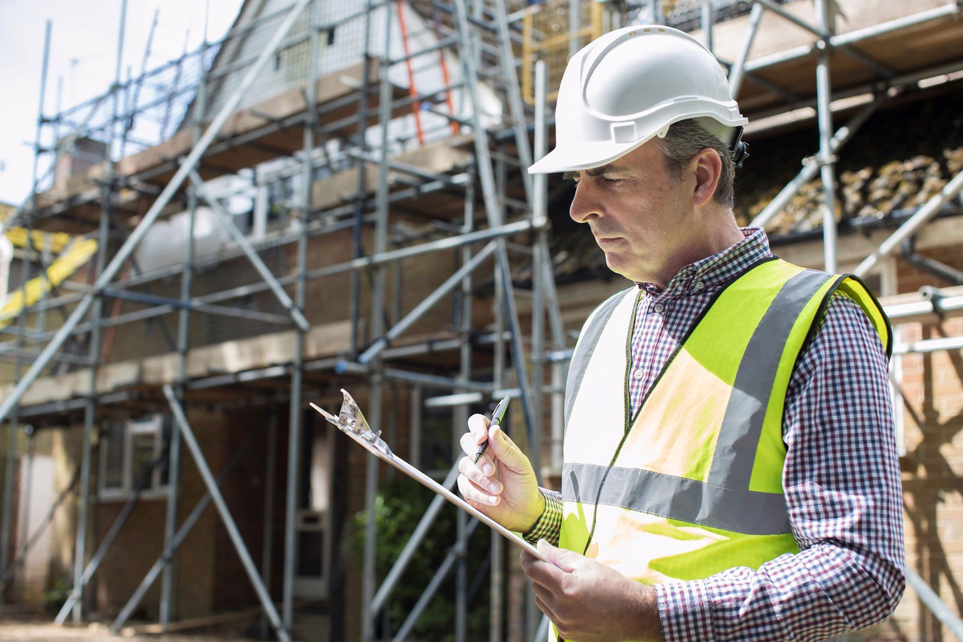 a construction worker is looking at a clipboard in front of a building under construction .