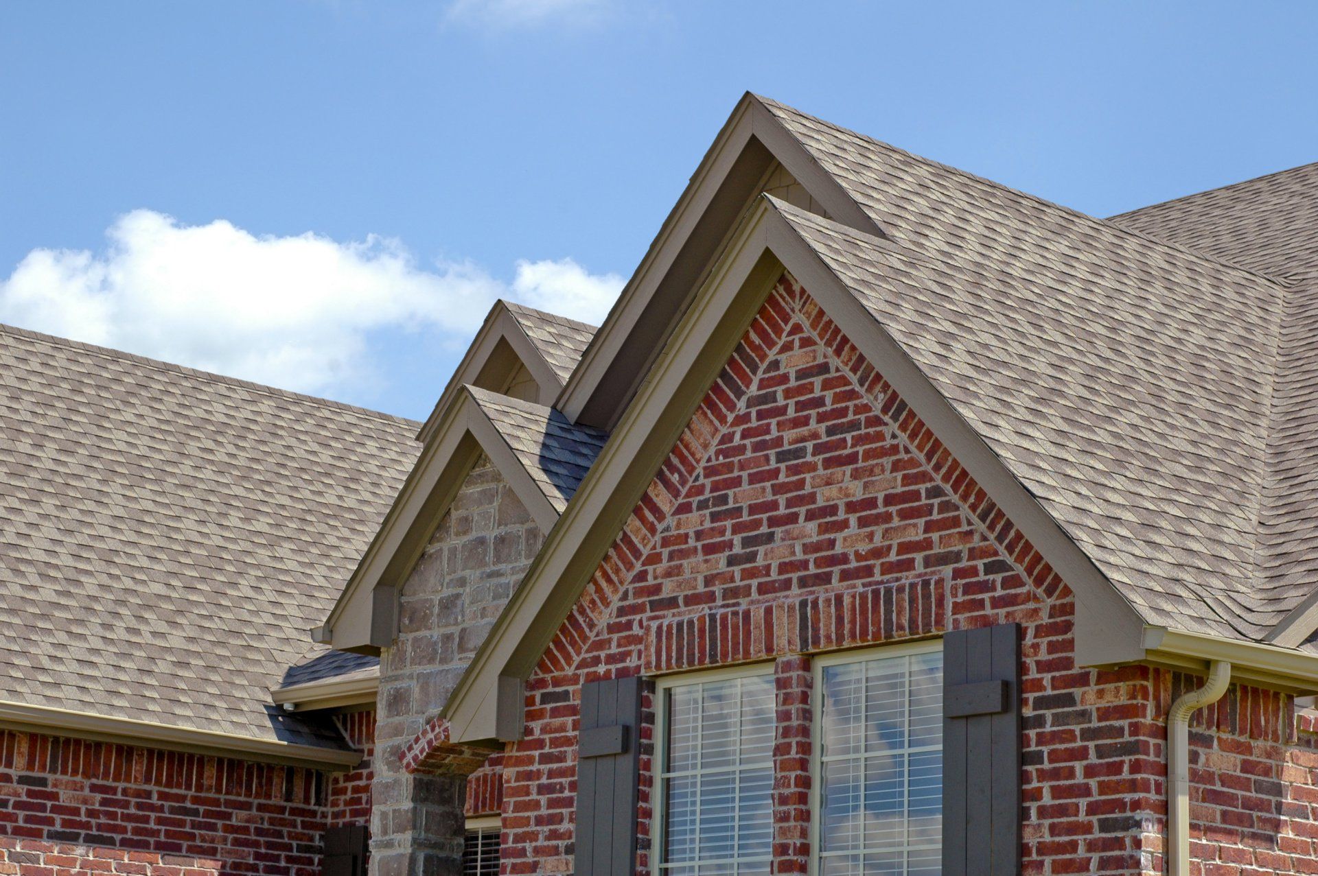 A brick house with a roof and a window with shutters.