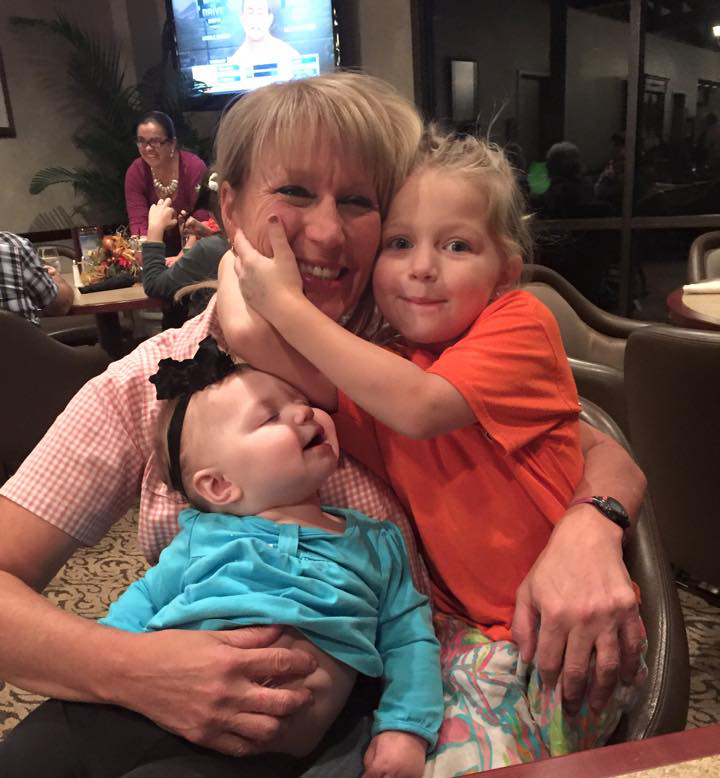 Woman holding two children at a restaurant, smiling while one child hugs her face.