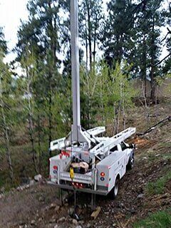 Utility truck with extended lift in a wooded area.