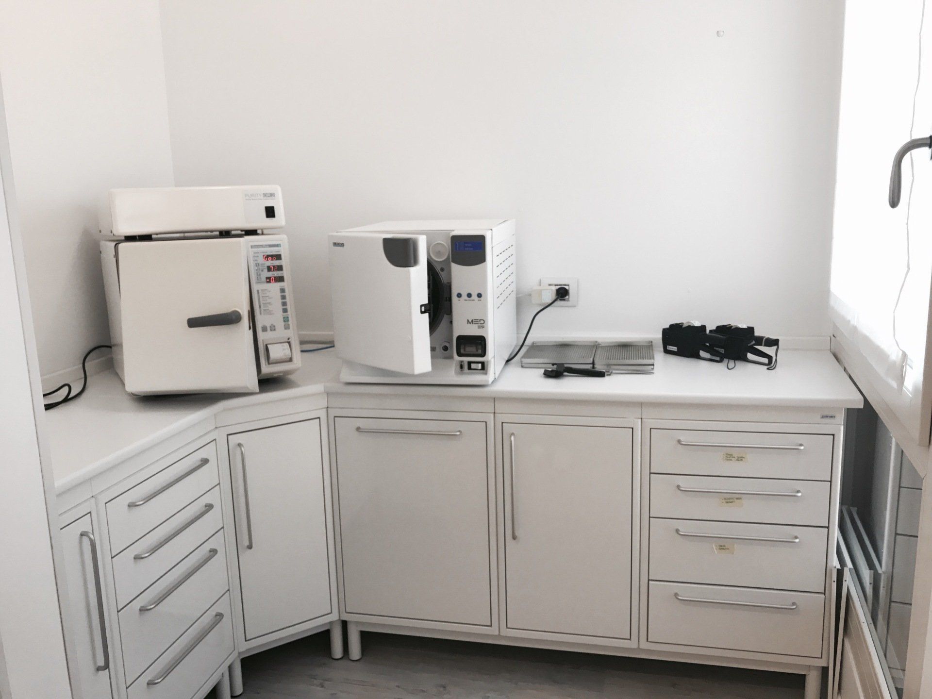 Attrezzature odontoiatriche bianche, compresi gli sterilizzatori, sono posizionate su un mobiletto bianco in un angolo dello studio dentistico.