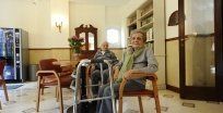 Due anziani seduti in un accogliente soggiorno con un deambulatore in primo piano.
