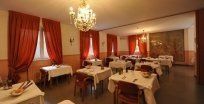 Elegante sala da pranzo di un ristorante con tovaglie bianche, tende rosse e un lampadario.
