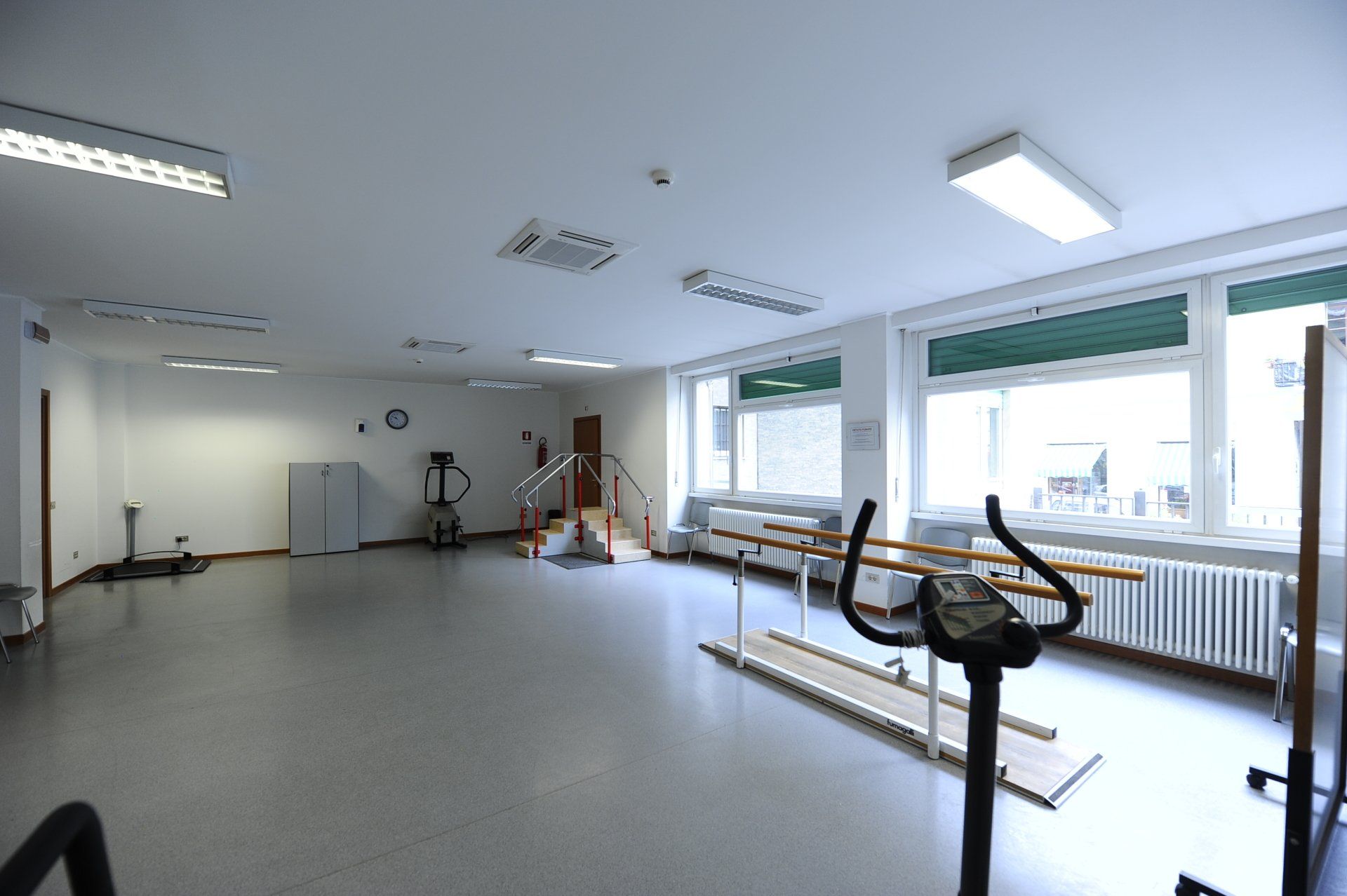 Luminosa palestra di riabilitazione vuota con sbarre per esercizi, attrezzature e grandi finestre.