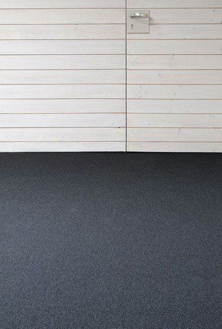 Ein schwarzer Teppichboden vor einer weißen Holzwand.