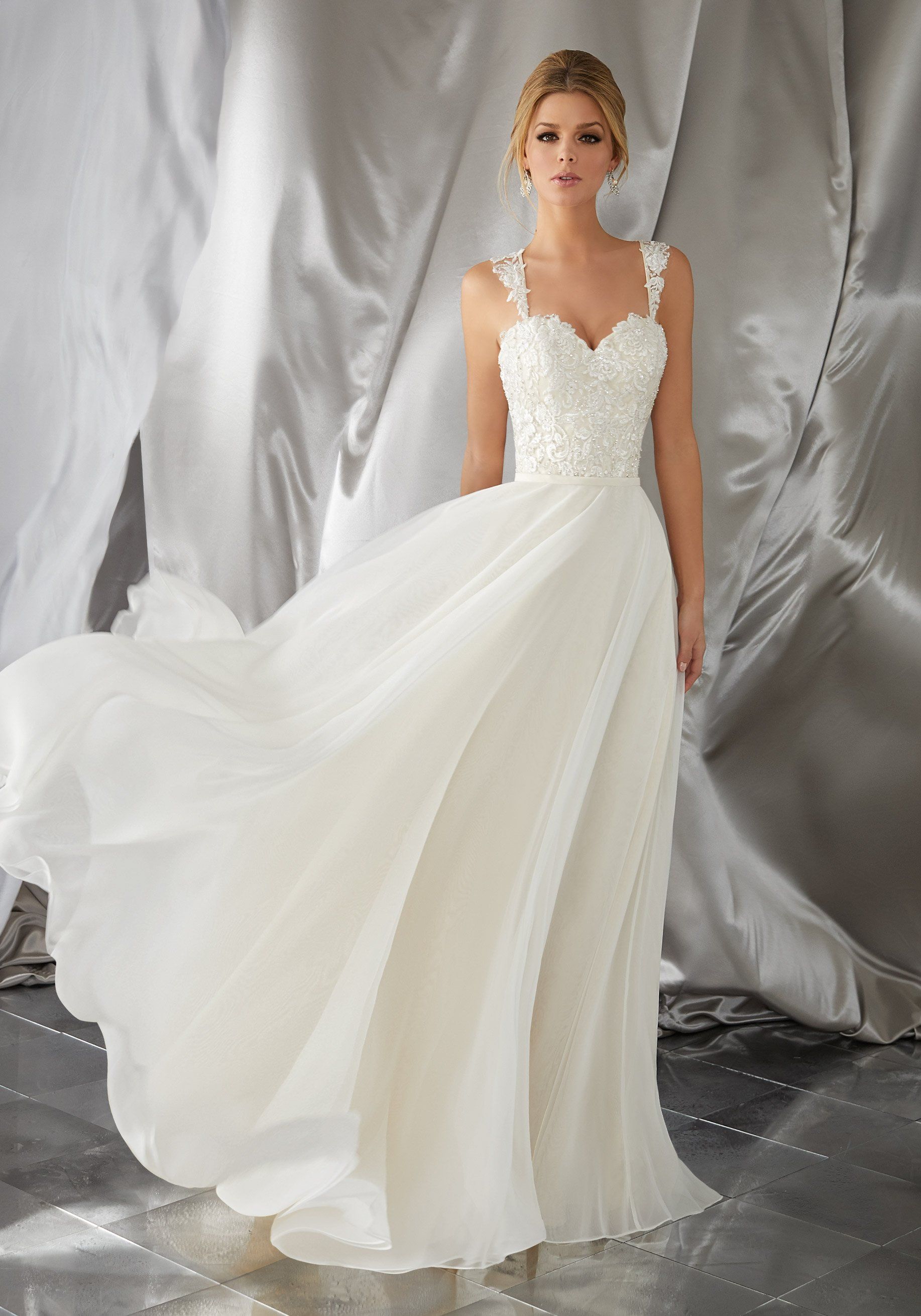 Eine Frau in einem weißen Brautkleid steht vor einem weißen Vorhang.