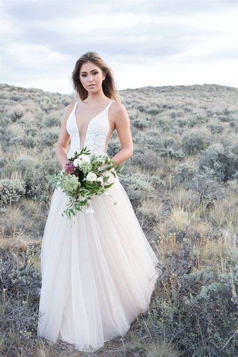 Eine Frau in einem Brautkleid steht mit einem Blumenstrauß in der Hand auf einem Feld.
