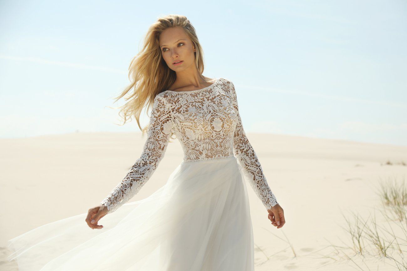 Eine Frau in einem weißen Spitzenkleid steht im Sand.