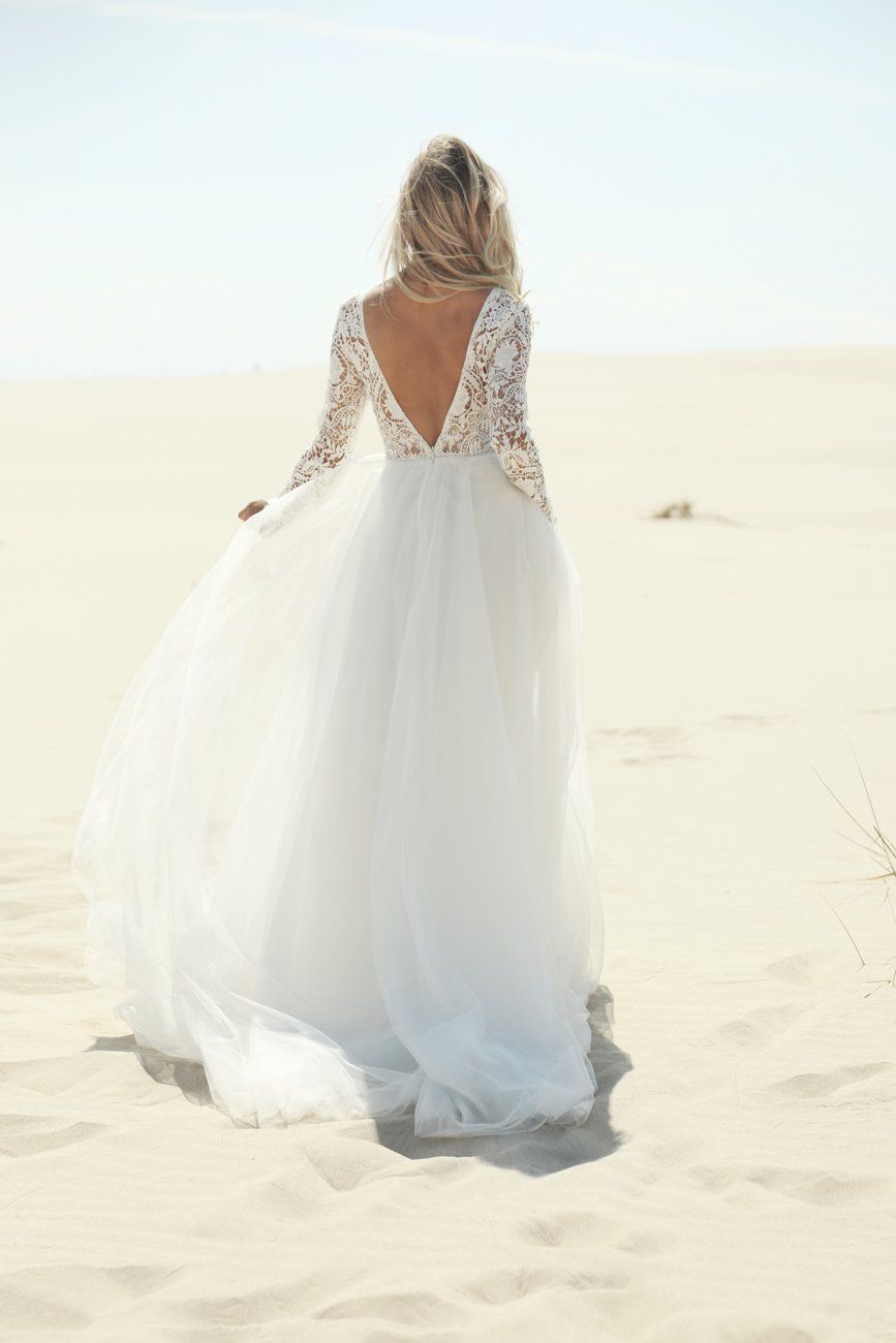 Eine Frau in einem weißen Brautkleid steht im Sand.