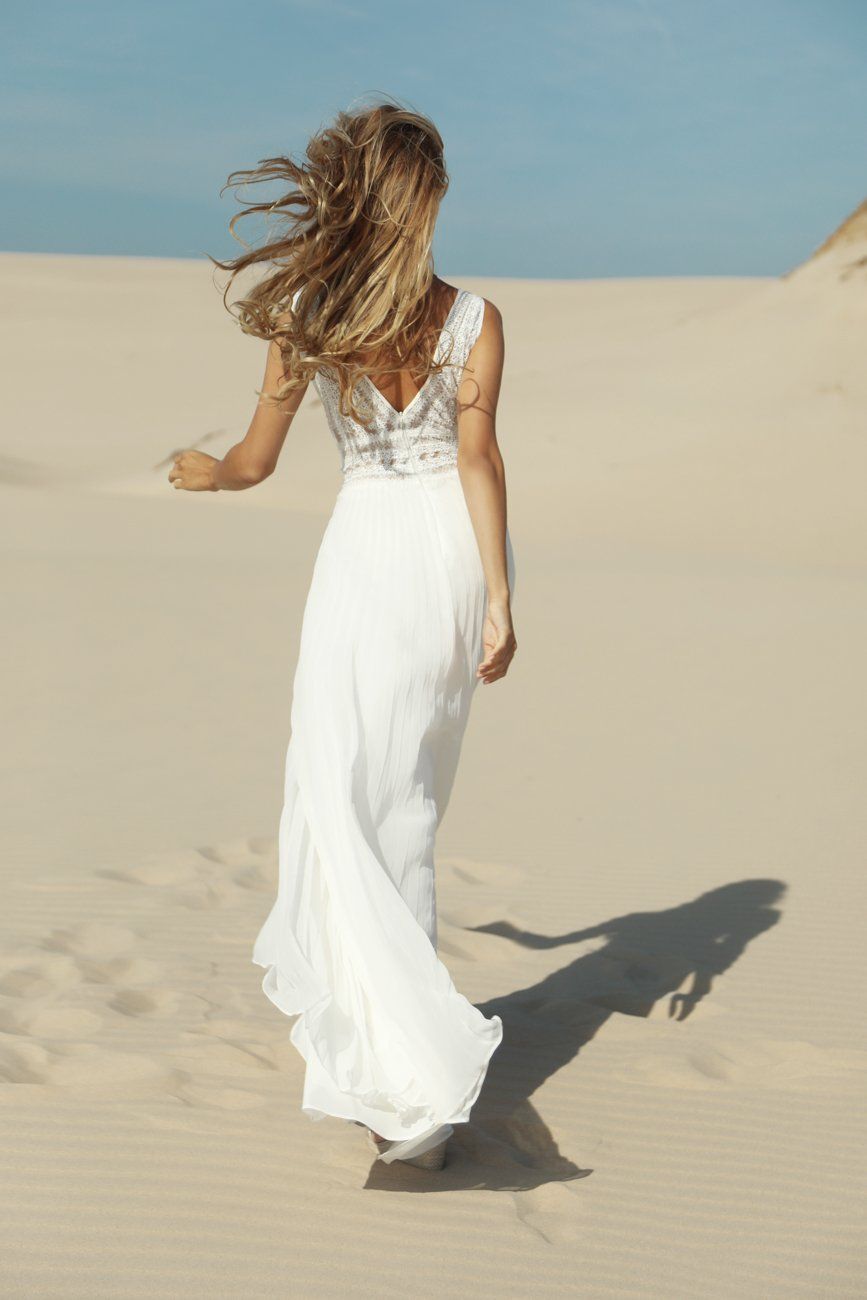 Eine Frau in einem weißen Kleid läuft im Sand.