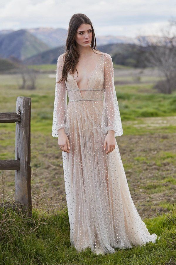 Eine Frau in einem Brautkleid steht auf einem Feld neben einem Holzzaun.