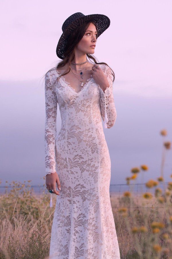 Eine Frau in einem weißen Spitzenkleid und Hut steht auf einem Feld.
