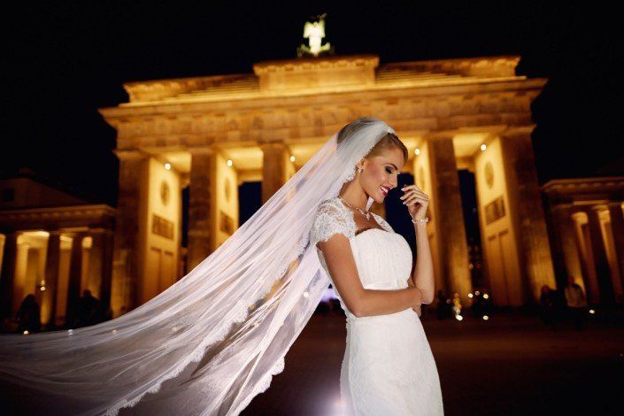 Eine Frau in einem Brautkleid und Schleier steht nachts vor einem Gebäude.