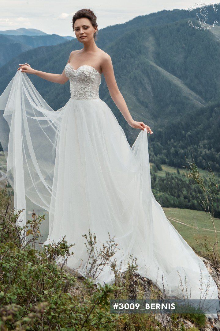 Eine Frau im Brautkleid steht auf einem Berggipfel und hält ihren Schleier.