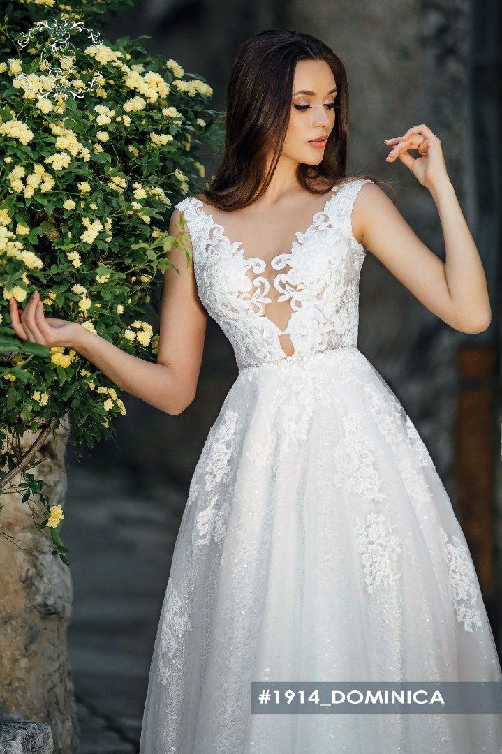 Eine Frau in einem weißen Brautkleid steht neben einem Busch mit gelben Blumen.