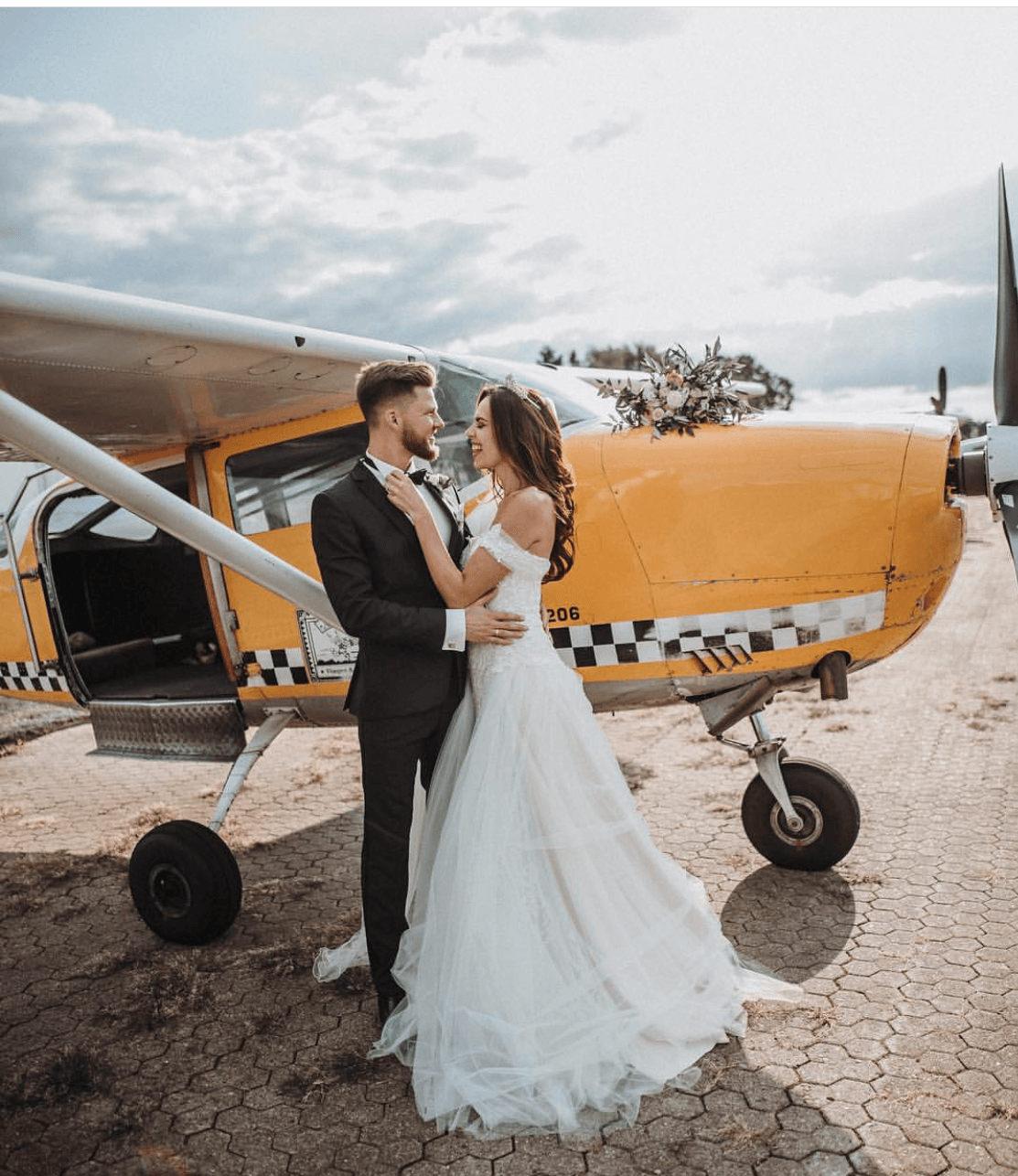 Eine Braut und ein Bräutigam posieren für ein Foto vor einem kleinen Flugzeug.
